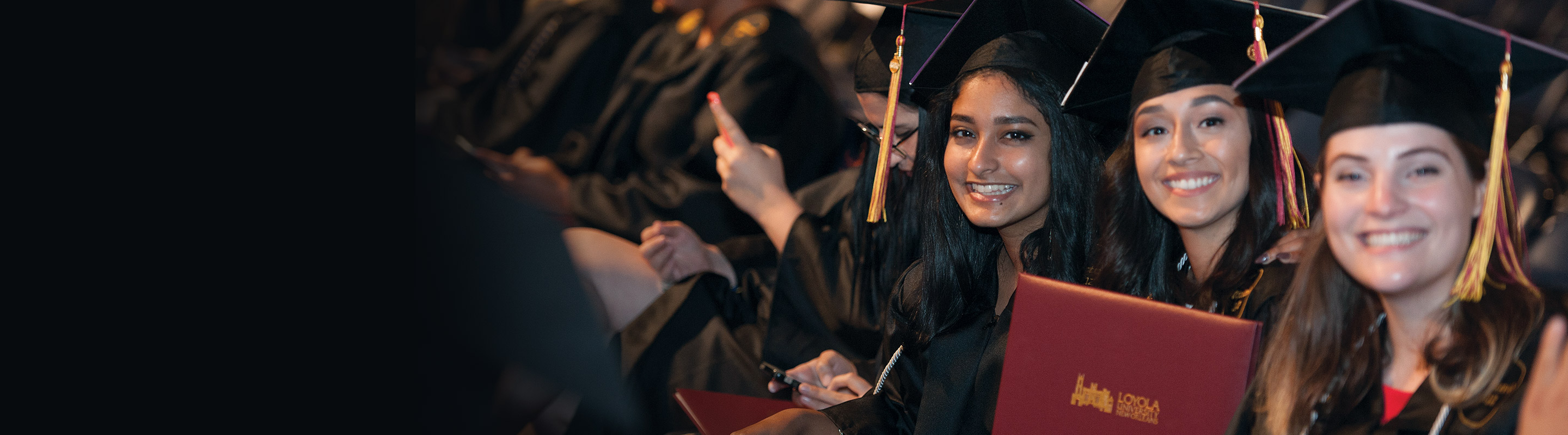 Students in regalia sitting at graduation with diplomas