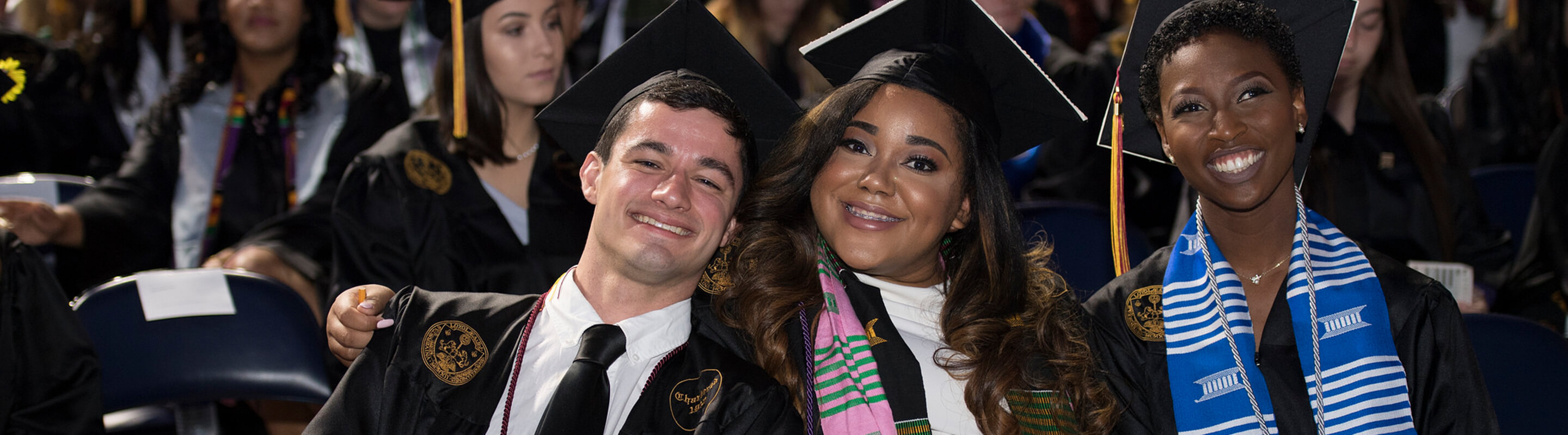 Three students in regalia sitting at commencement