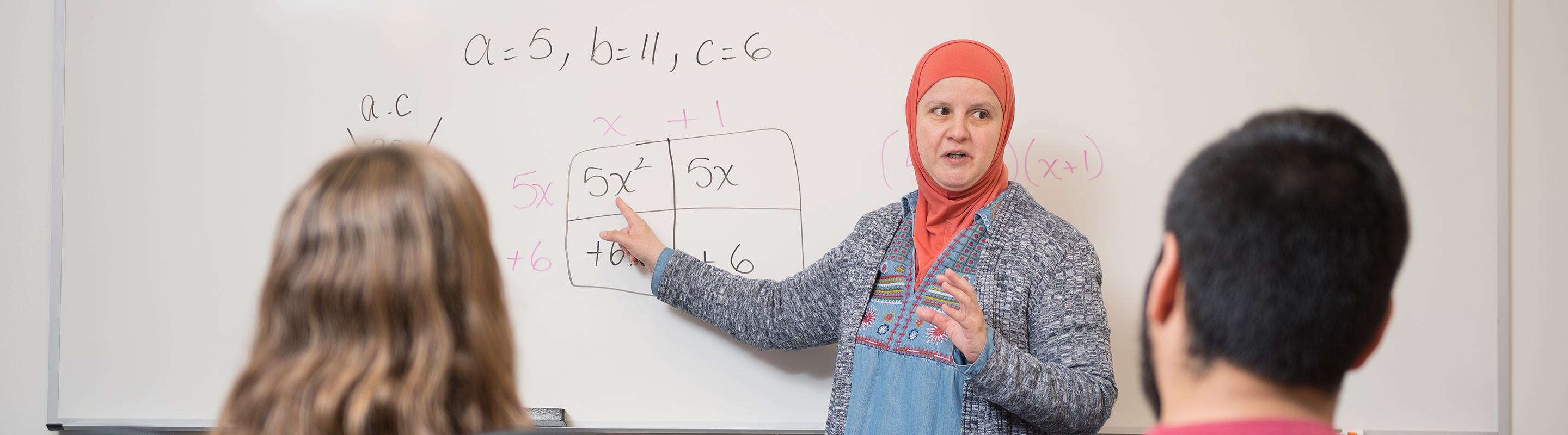 Dr. Sarmini instructing three students on solving an equation on a whiteboard