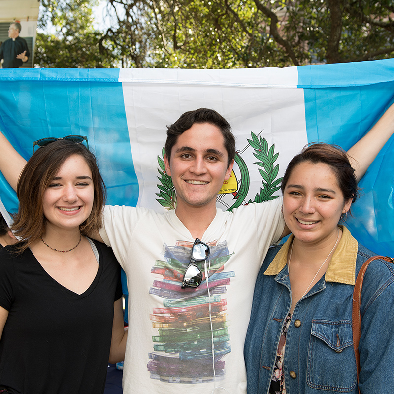Three students standing in front of flag