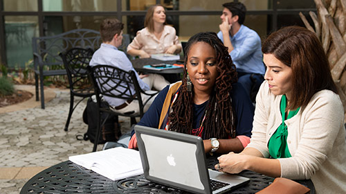 Two students looking at laptop on outdoor table